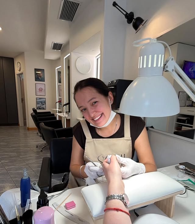 Stylist in a white apron smiling at the nail station